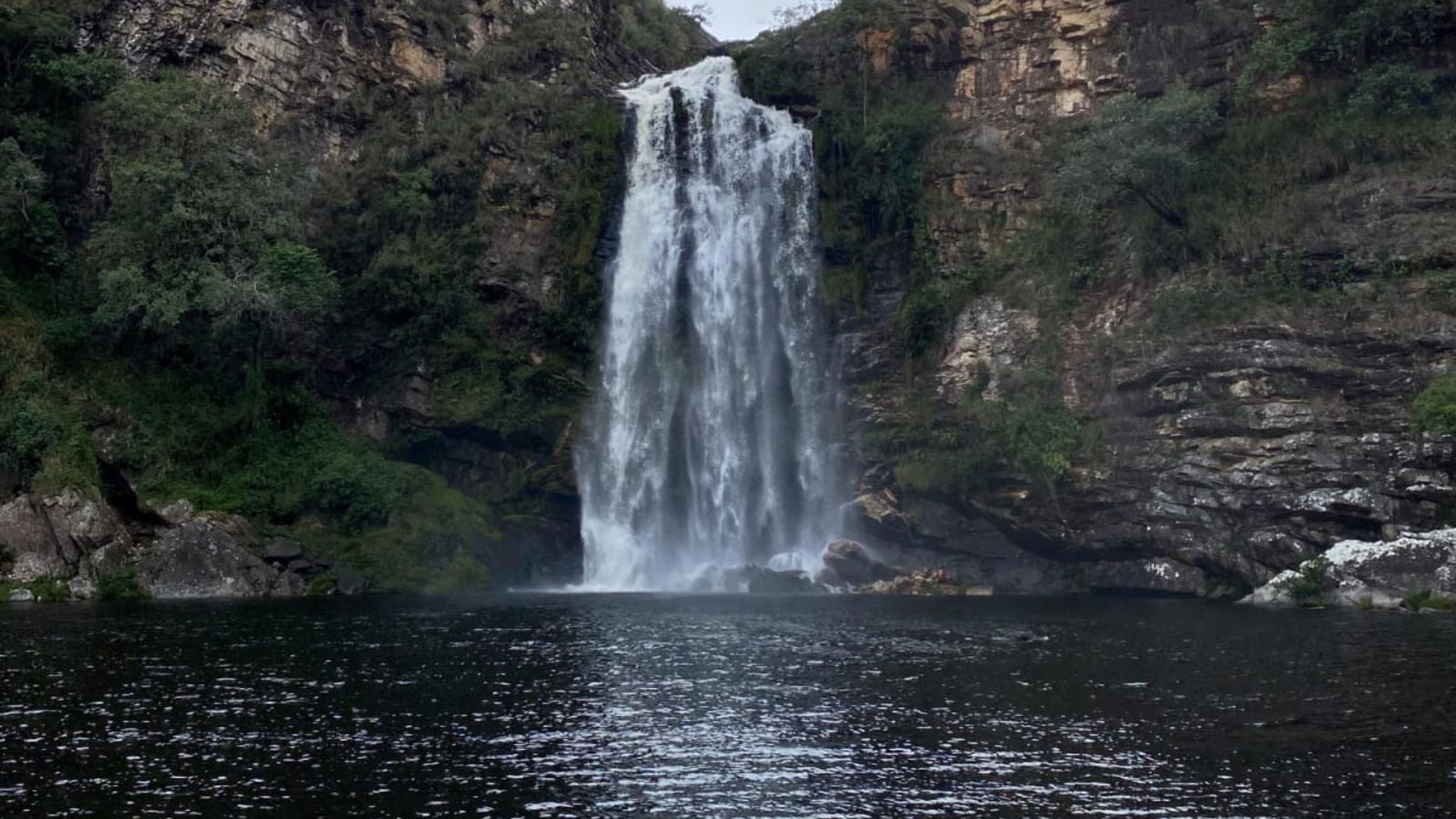 Cachoeira entre paredões rochosos e vegetação, com um poço de água na base