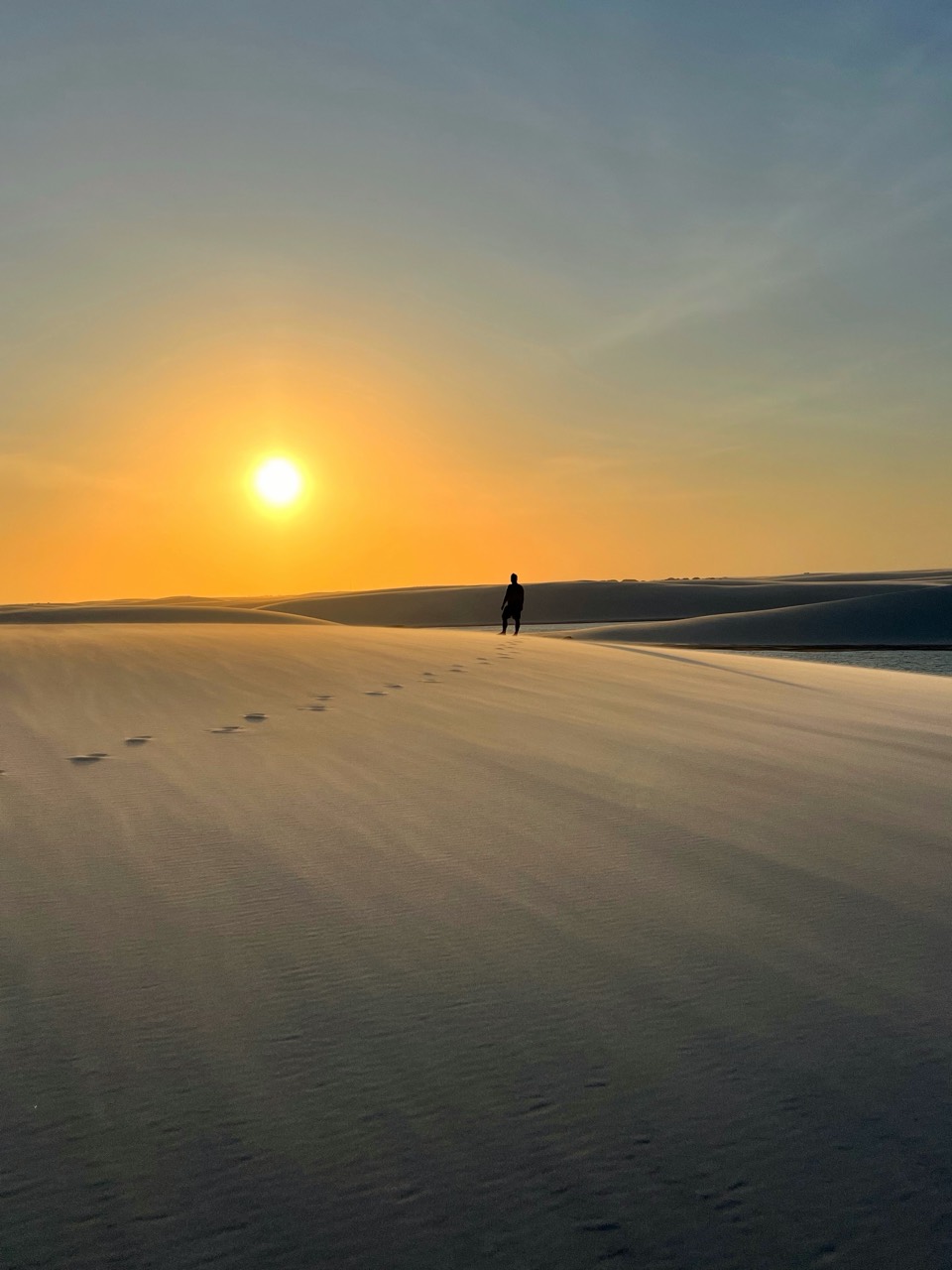 Pôr do sol nas dunas dos Lençóis Maranhenses, com caminhante e pegadas na areia